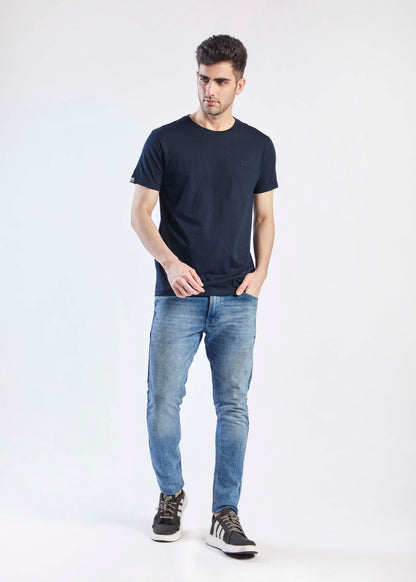 Man wearing a navy t-shirt and light blue jeans on a white background full pose